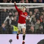 Alejandro Garnacho of Manchester United celebrating, pointing upwards with his right hand outstretched, with a ball under his left arm, running with the goal behind him.