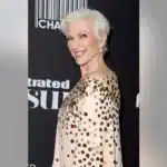 Maye Musk looking to the side and smiling in a gold and beige sparkling dress.